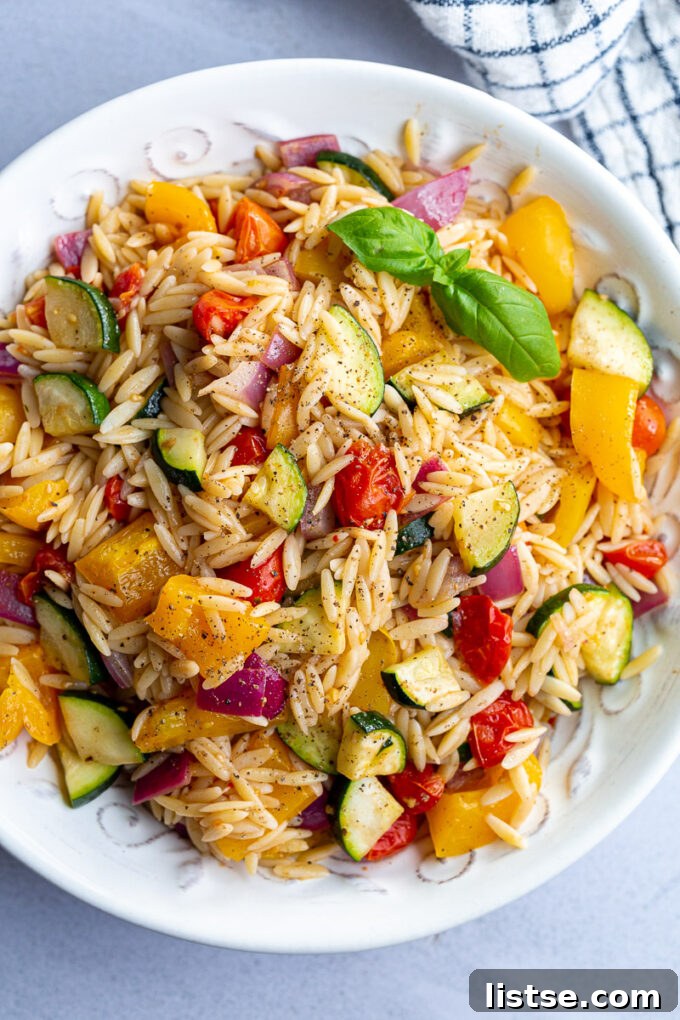 Orzo pasta salad with roasted veggies mixed in, garnished with fresh herbs.