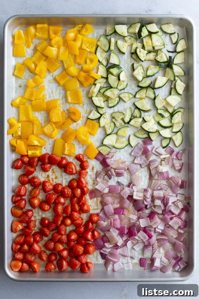 Roasted bell pepper, zucchini, red onion, and cherry tomatoes on a baking tray after roasting.