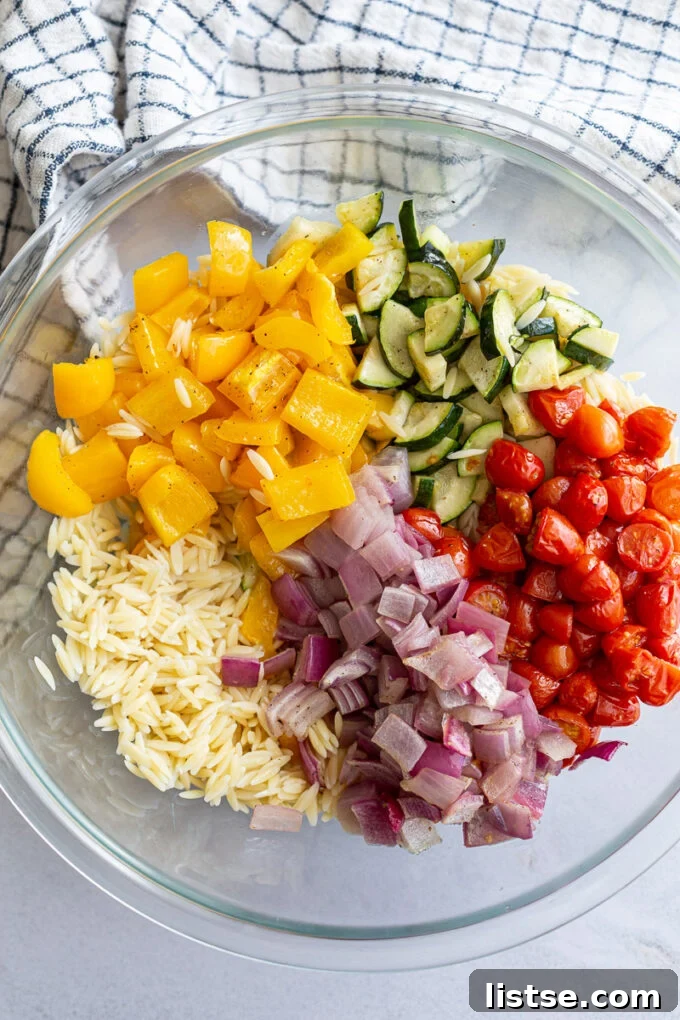 Tossing orzo pasta with roasted veggies and dressing in a large bowl.