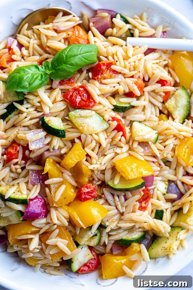 Close-up of zucchini, bell pepper, and red onion tossed with orzo pasta in a bowl.