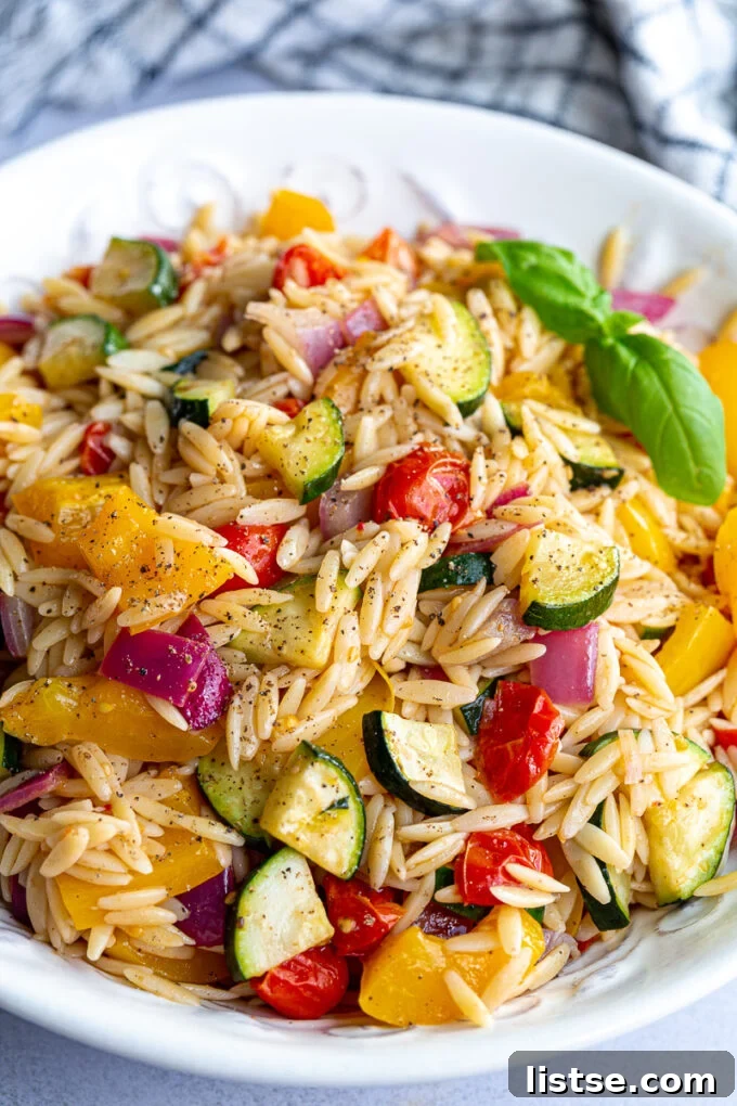 Roasted vegetable pasta salad topped with fresh basil leaves in a white bowl.