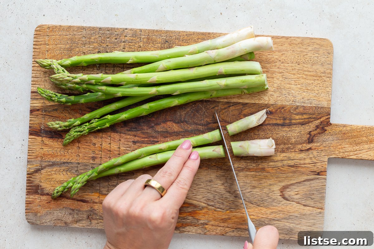Speedy Skillet Asparagus 5 asparagus on a wood cutting board with a hand cutting off the woody ends of the asparagus