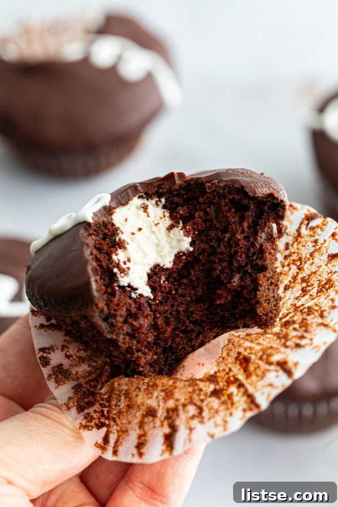 Close-up of a vegan Hostess-style cupcake with a bite taken, revealing the luscious cream filling and chocolate ganache