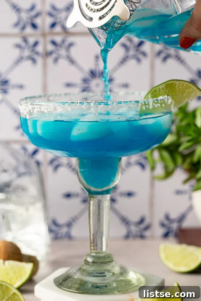 Ocean Breeze Margarita 4 A vibrant blue cocktail being poured from a shaker into a margarita glass filled with ice.