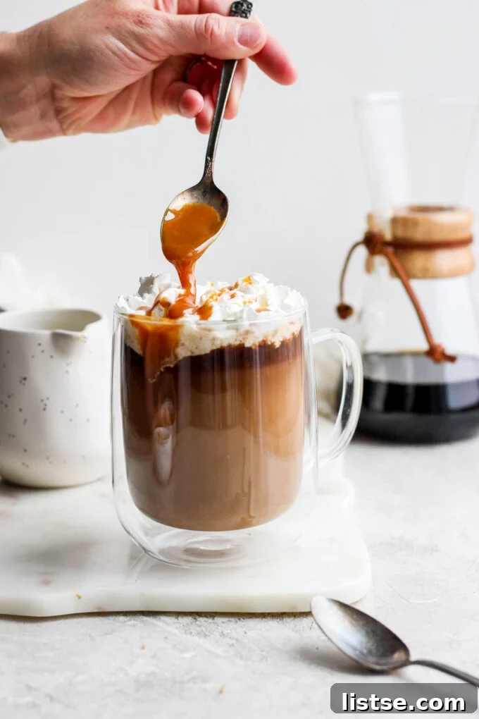 Velvet Caramel Dream 7 A hand adding a final drizzle of rich caramel sauce over the top of a finished caramel latte.