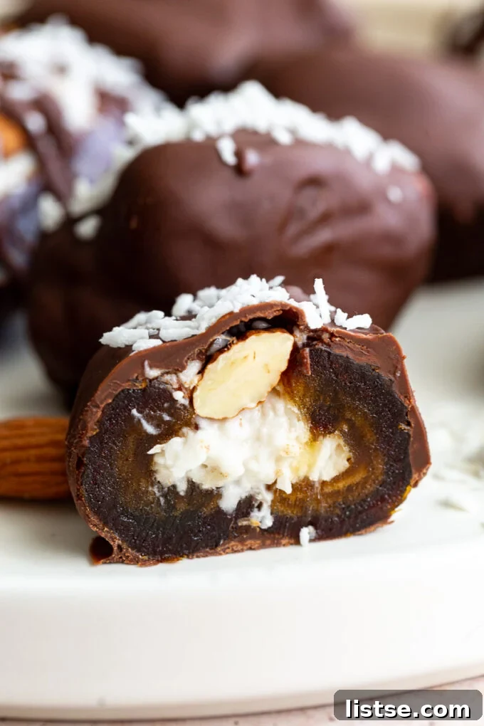 A Medjool date cut in half, revealing the soft coconut filling inside, with a whole almond and chocolate topping.