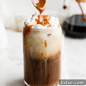 Using a spoon to drizzle caramel over the top of an iced latte.