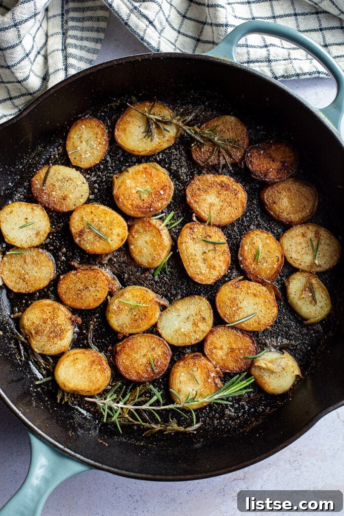 Rosemary pan-fried potato coins sizzling in a cast iron skillet