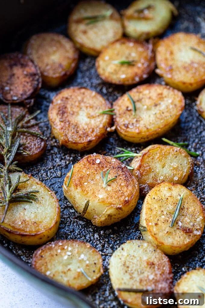 Sautéed potato coins generously garnished with fresh rosemary in a cast iron skillet