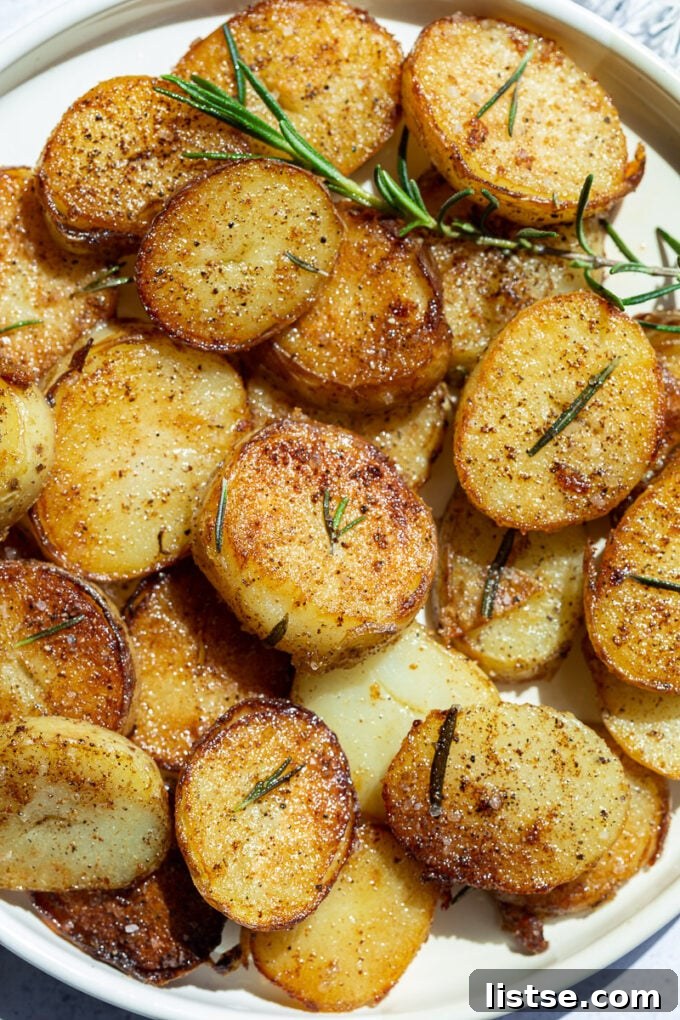 A plate of perfectly crispy fried potatoes garnished with fresh rosemary