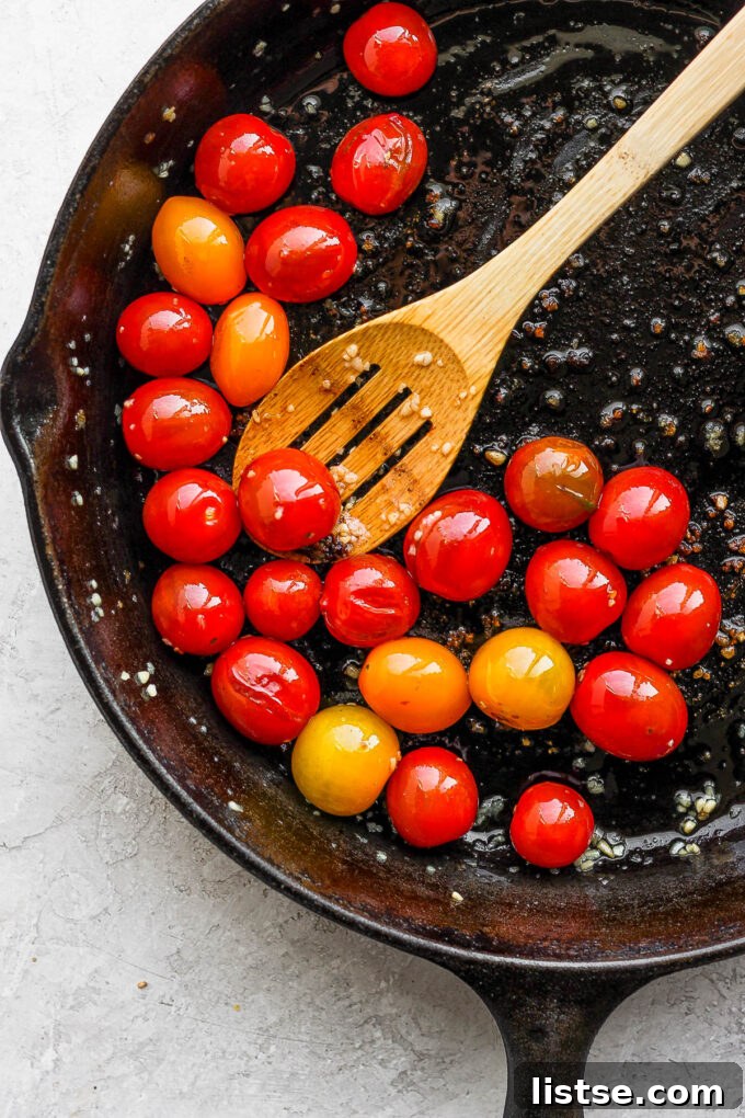 Cherry tomatoes gently cooking and bursting in a skillet with olive oil and garlic.