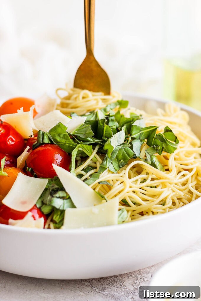 Pasta served in a white bowl with vibrant cherry tomatoes, fresh basil, and grated Parmesan cheese, glistening with olive oil.