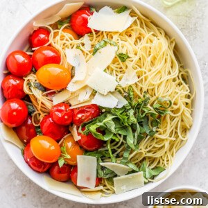 White bowl filled with pasta, tomatoes, basil and parmesan cheese.