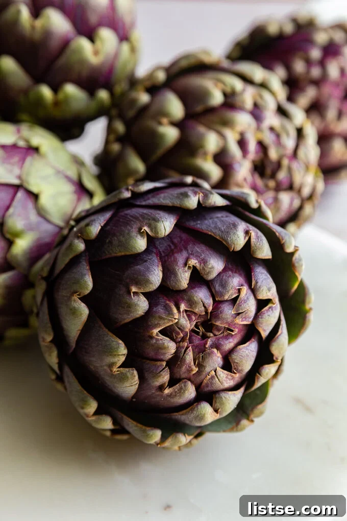 Gourmet Stuffed Purple Artichokes 5 Freshly trimmed purple artichokes laid out on a cutting board, ready for the next step in preparation.