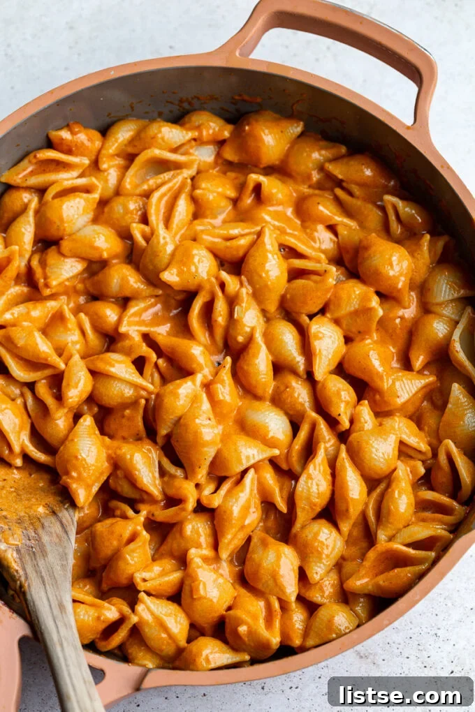 A close-up of pasta and creamy vodka sauce being stirred together in a large skillet, steam rising.