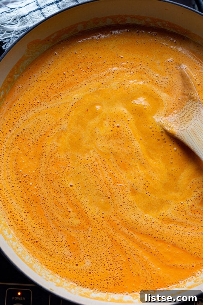 Stirring vibrant red pepper pasta sauce in a large pot before adding pasta.
