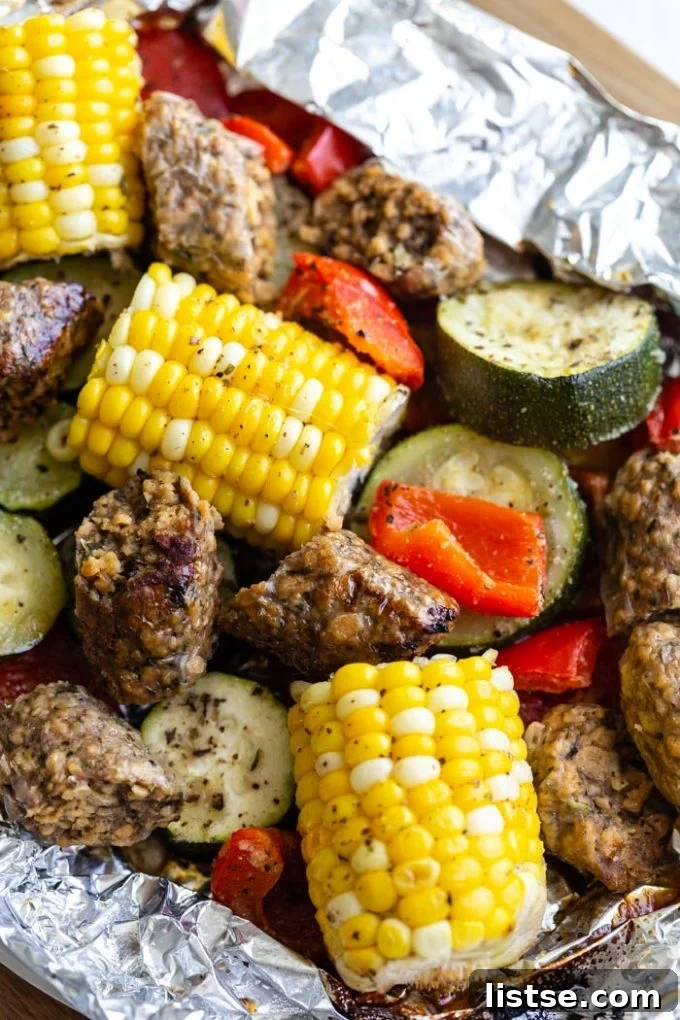 Sizzling Vegetarian Grills 8 An open foil pack revealing perfectly cooked corn on the cob, vegan sausage, and other fresh vegetables, a complete meal.