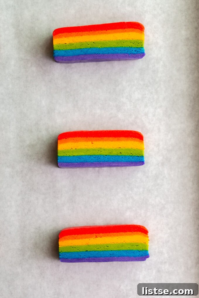 Carefully rolled out layers of colored vegan cookie dough, separated by parchment paper, showcasing the preparation process.