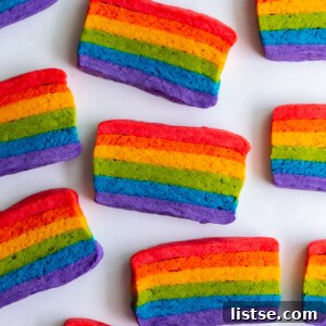 A high-angle view of perfectly baked Vegan Pride Flag Sugar Cookies, showcasing the vibrant rainbow layers, on a white surface.