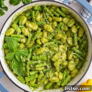 Pesto gnocchi in a large skillet, garnished with fresh basil and lemon, captured in a square format.