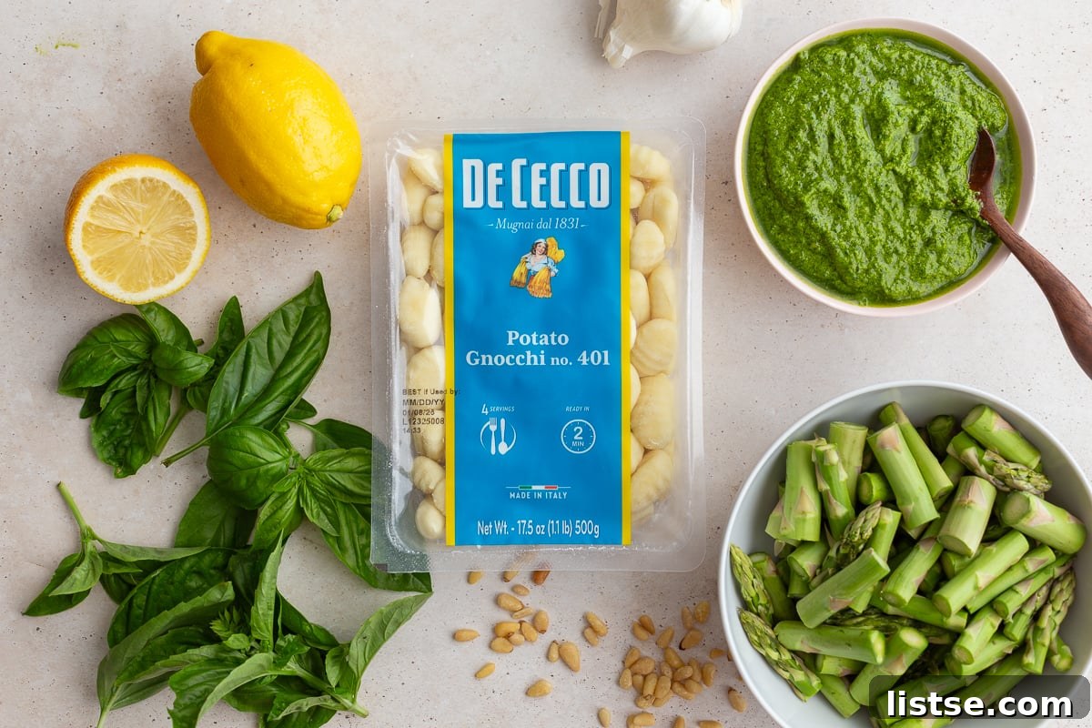 Key ingredients for making pesto gnocchi laid out: store-bought gnocchi, fresh basil pesto, a whole lemon, and fresh asparagus spears.
