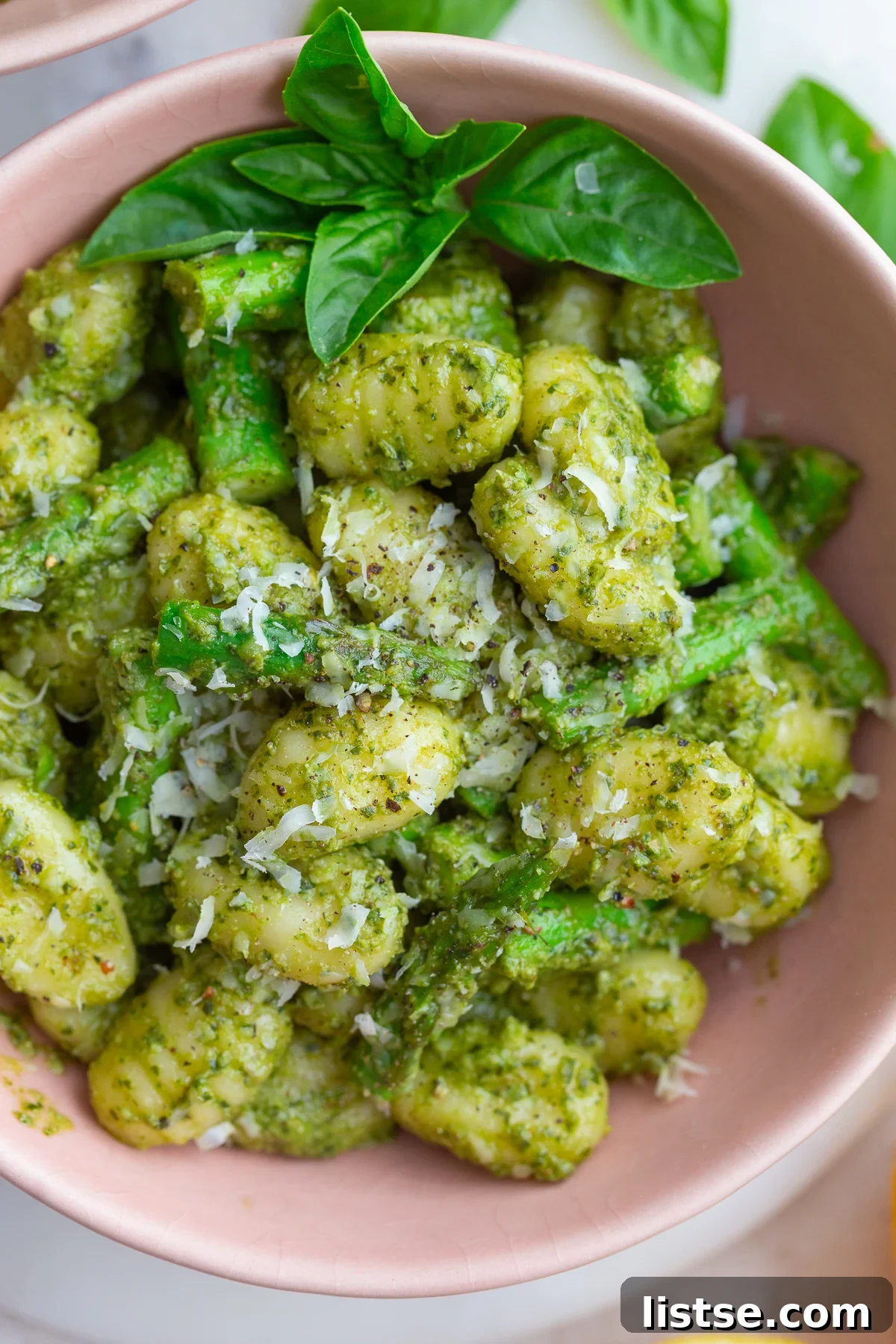 A large bowl filled with freshly made pesto gnocchi, garnished with fresh basil leaves and lemon wedges on the side, ready for serving.