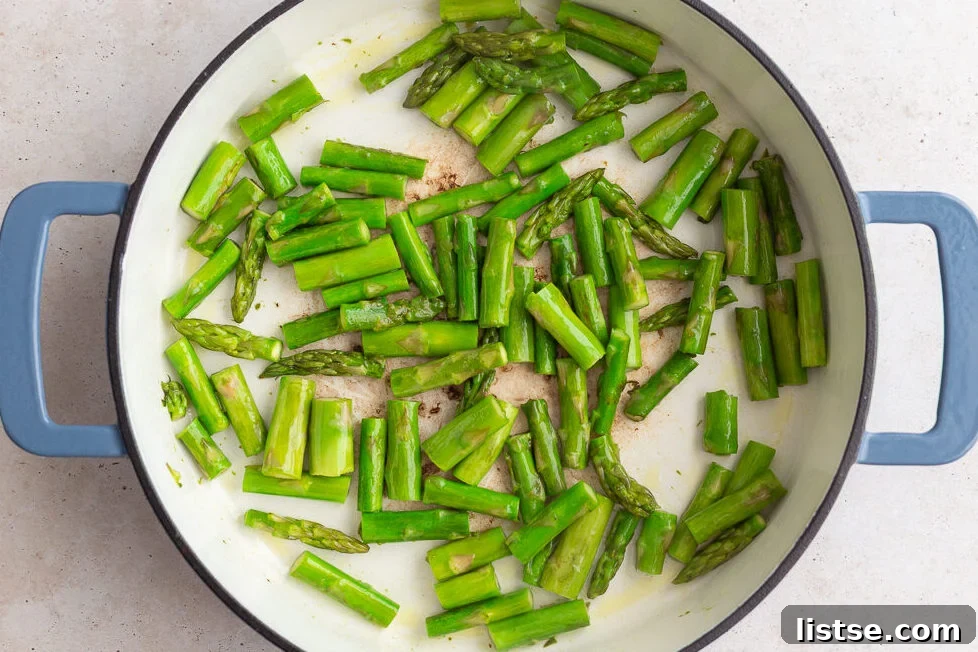 Asparagus pieces being sautéed in a large non-stick skillet over medium heat.