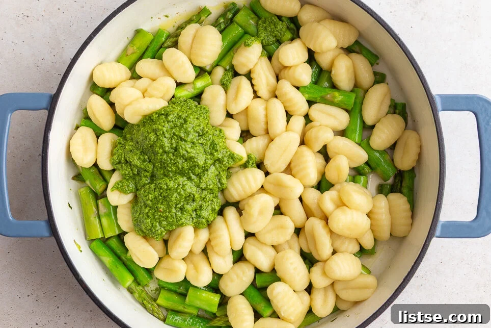 Cooked gnocchi and fresh pesto being added to a skillet with sautéed asparagus, ready to be combined.