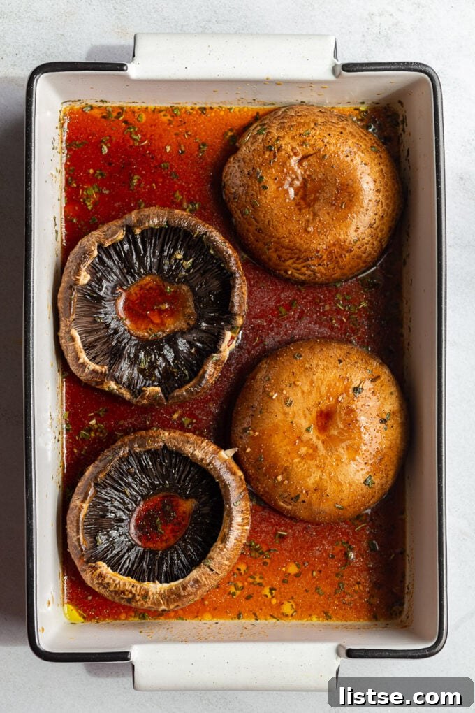 Portobello mushrooms soaking in a rich, dark marinade within a shallow dish, absorbing flavors.