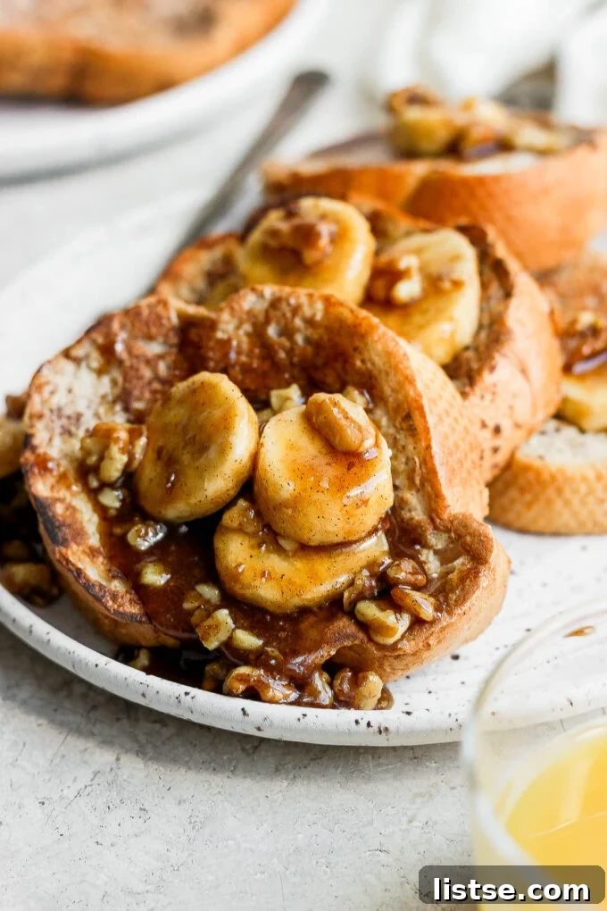 Close-up of French toast topped with caramelized bananas, chopped nuts, and a dusting of powdered sugar.