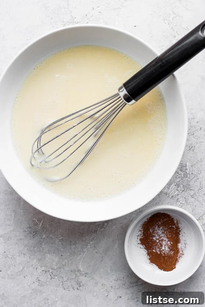 Hands whisking an egg custard mixture in a shallow white dish.
