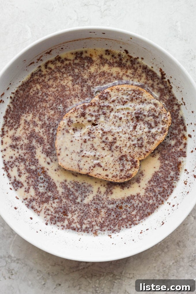 A slice of thick bread being dipped into a shallow dish of egg custard.