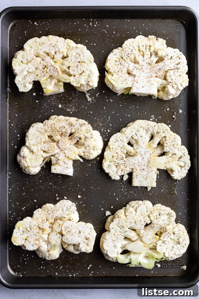 Savory Cauliflower Cutlets 3 Two raw, whole cauliflower heads resting on a large baking sheet, prepared for slicing into uniform steaks.