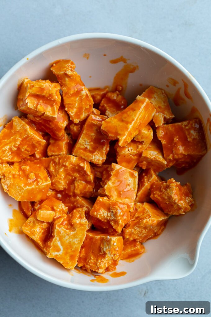 Tofu chunks in a bowl marinating in buffalo sauce, ready for the next step.