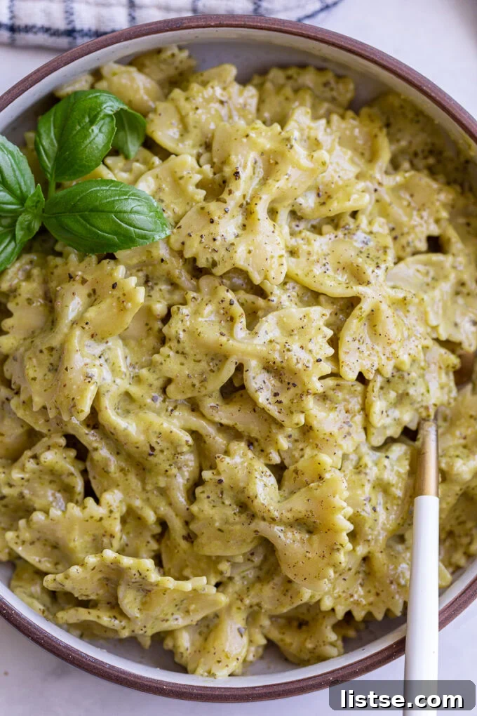 A bowl of delectable pasta coated in creamy pesto sauce, garnished with fresh basil.