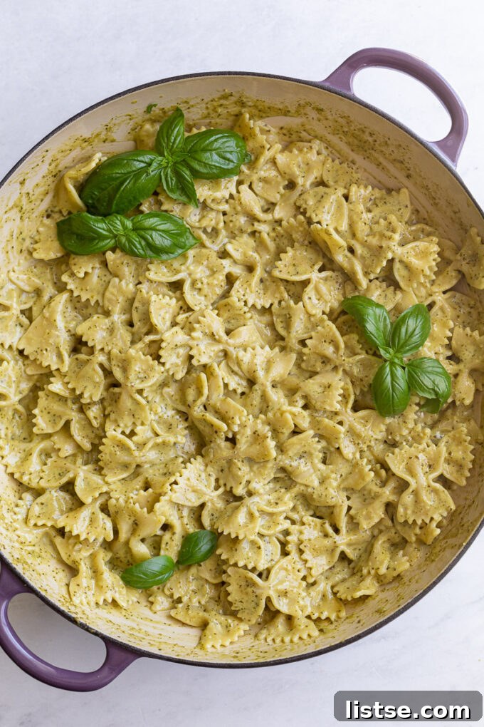 Cooked pasta generously coated in pesto cream sauce, garnished with fresh basil leaves in a large skillet.