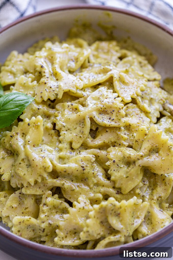 A close-up shot of perfectly cooked bowtie pasta (farfalle) with a rich pesto cream sauce.