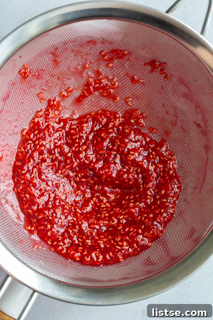 Straining out seeds from cooked raspberries in a sieve. 