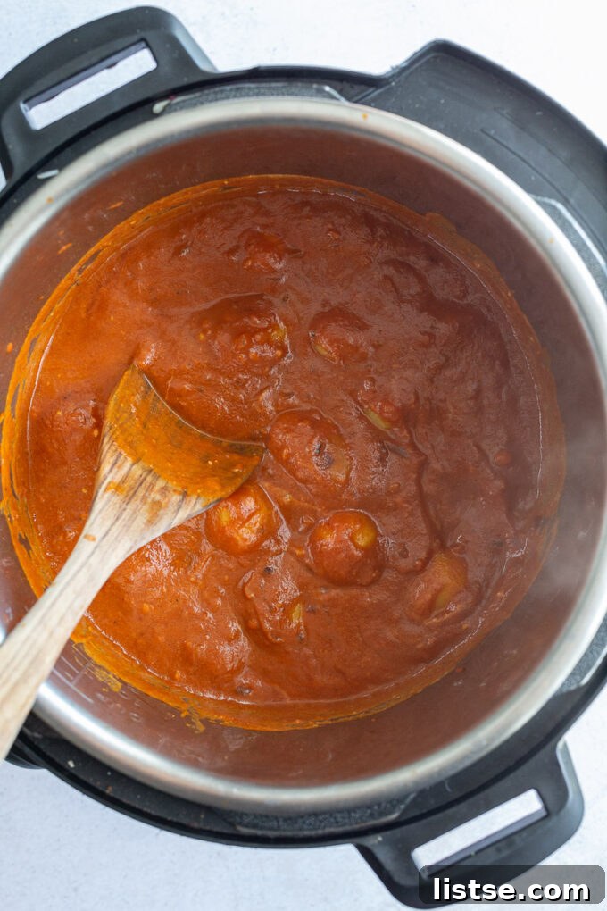 A close-up of a hand gently stirring tender baby potatoes into the rich, aromatic tomato sauce in an Instant Pot.
