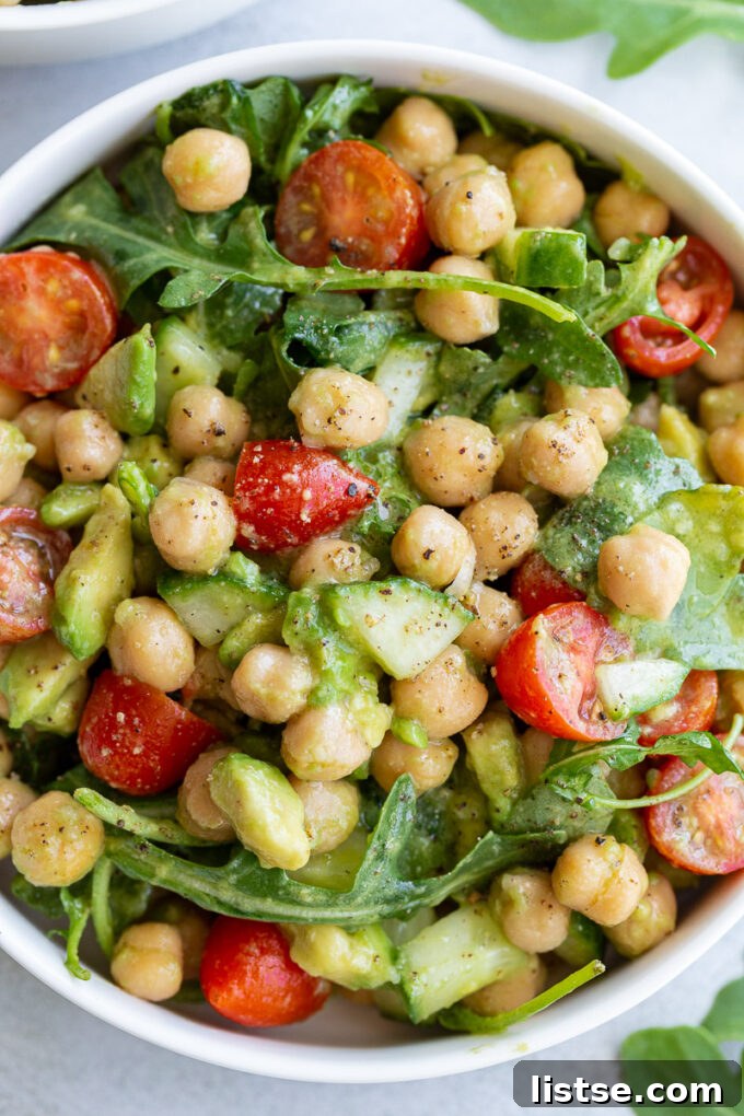 A close-up view of the ingredients for Chickpea Avocado Salad, showing chickpeas, diced avocado, cherry tomatoes, cucumber, and fresh arugula mixed together.