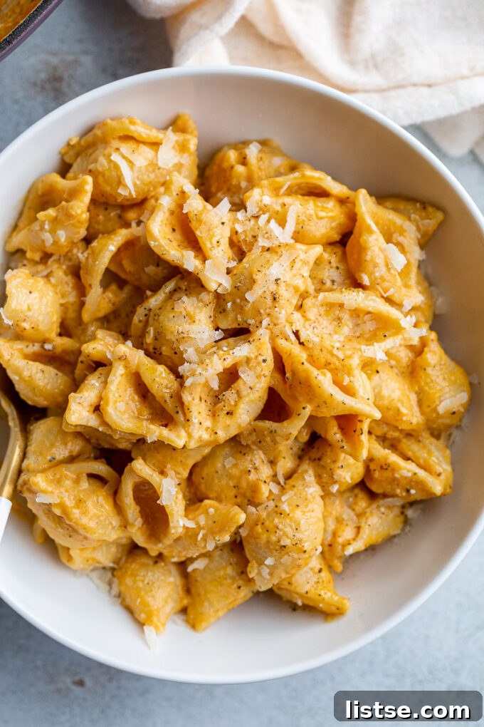 A close-up shot of creamy pumpkin macaroni pasta generously topped with shredded parmesan cheese, ready to be served.