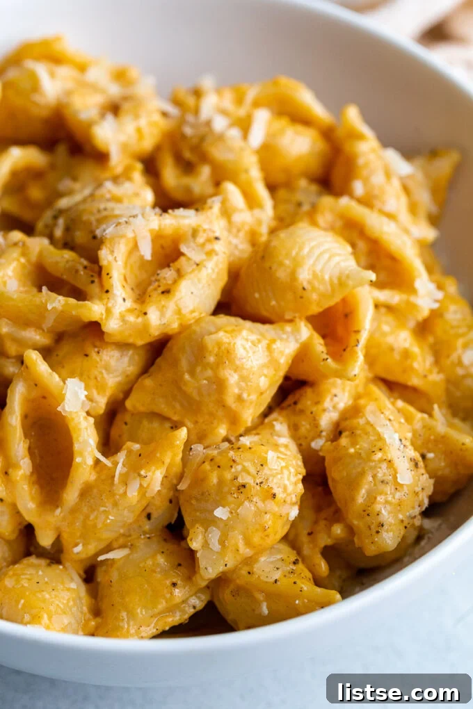Close-up of creamy pumpkin macaroni pasta, garnished with fresh herbs and a generous sprinkle of grated parmesan cheese.