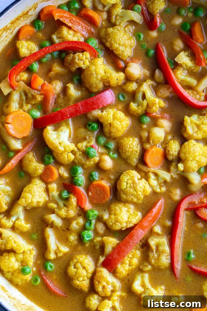 Cauliflower and various colorful vegetables cooking in a large skillet, coated in a creamy curry sauce.