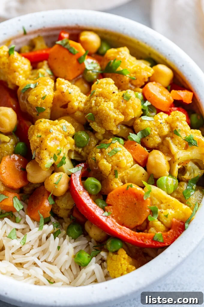A bowl of creamy cauliflower curry served with a side of white rice, garnished with fresh herbs.