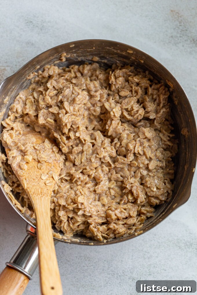 Spiced Morning Oats 4 A wooden spoon stirring creamy cinnamon oatmeal in a saucepan on the stove, illustrating the cooking process.