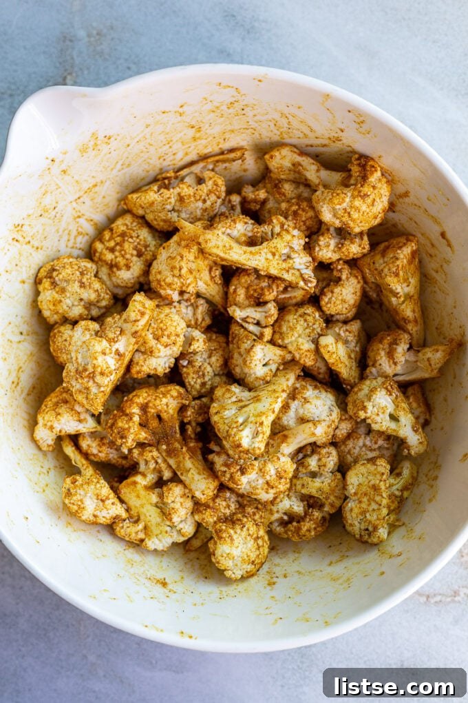 Seasoning cauliflower florets in a bowl with spices.