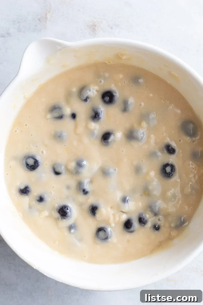 Bright Lemon Blueberry Muffins 4 Mixing fresh blueberries with muffin batter in a large mixing bowl.