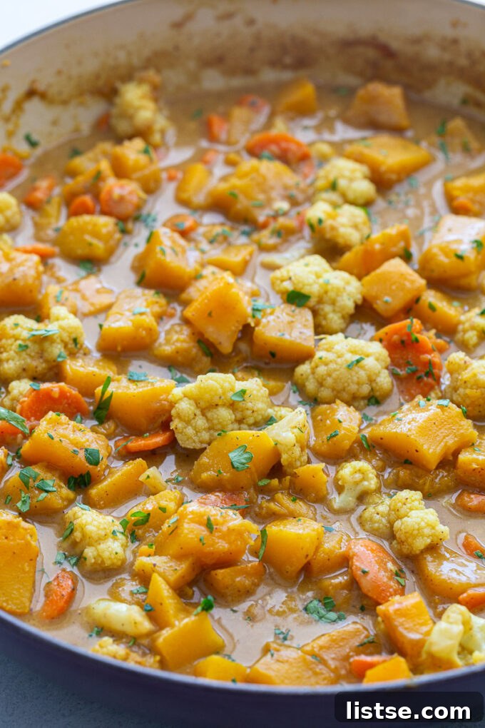 Freshly chopped pumpkin and cauliflower florets cooking in a large skillet, coated in a vibrant curry sauce, showcasing the rich colors of the ingredients.