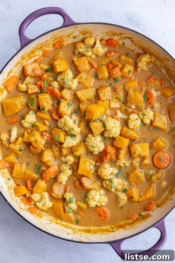 A close-up of the vegan pumpkin curry simmering in a large skillet, showing the creamy texture of the sauce and the tender vegetables.