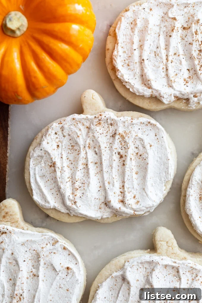 pumpkin shaped sugar cookies topped with a maple icing and sprinkled with nutmeg. a small orange pumpkin in the corner